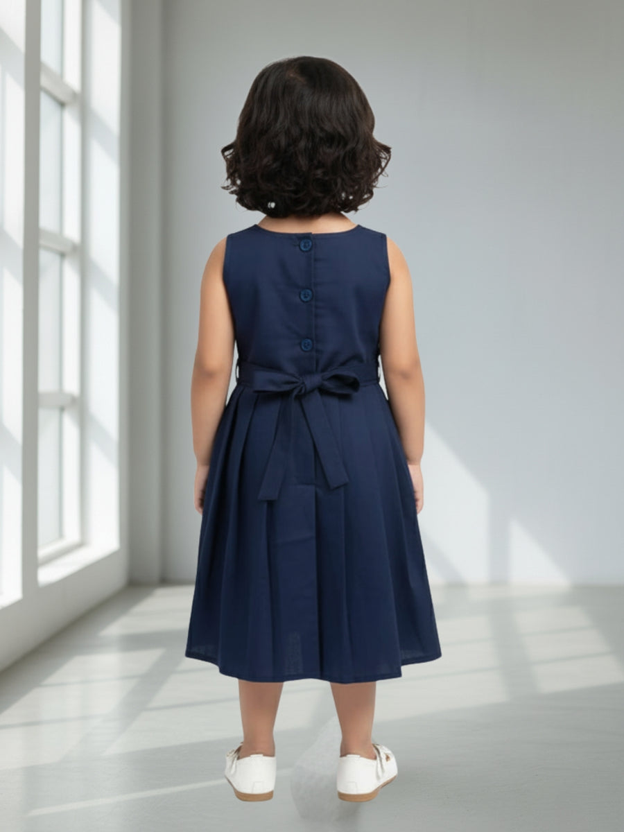 Child wearing a navy blue dress with a bow detail in a bright room.
