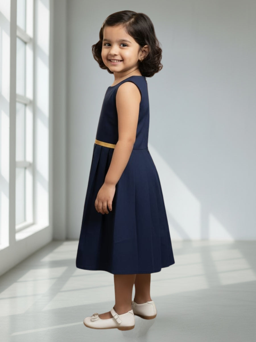 Young girl wearing a navy dress with a gold belt in a bright room.