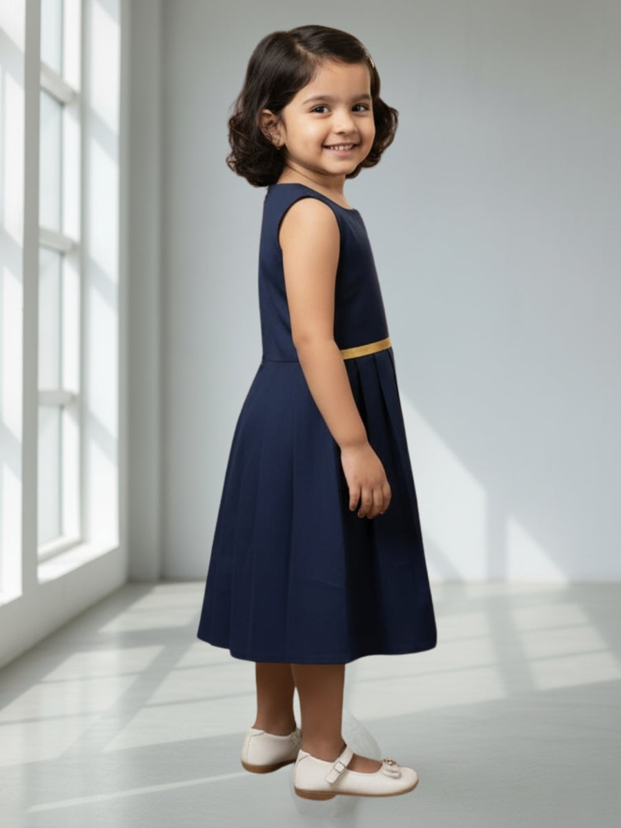 Young girl wearing a navy dress with a gold belt in a bright room.