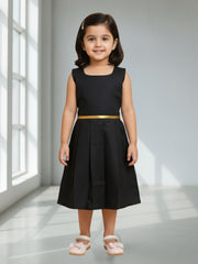 Young girl wearing a black dress with a gold belt in a bright room.