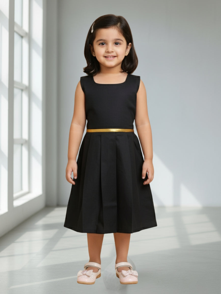 Young girl wearing a black dress with a gold belt in a bright room.