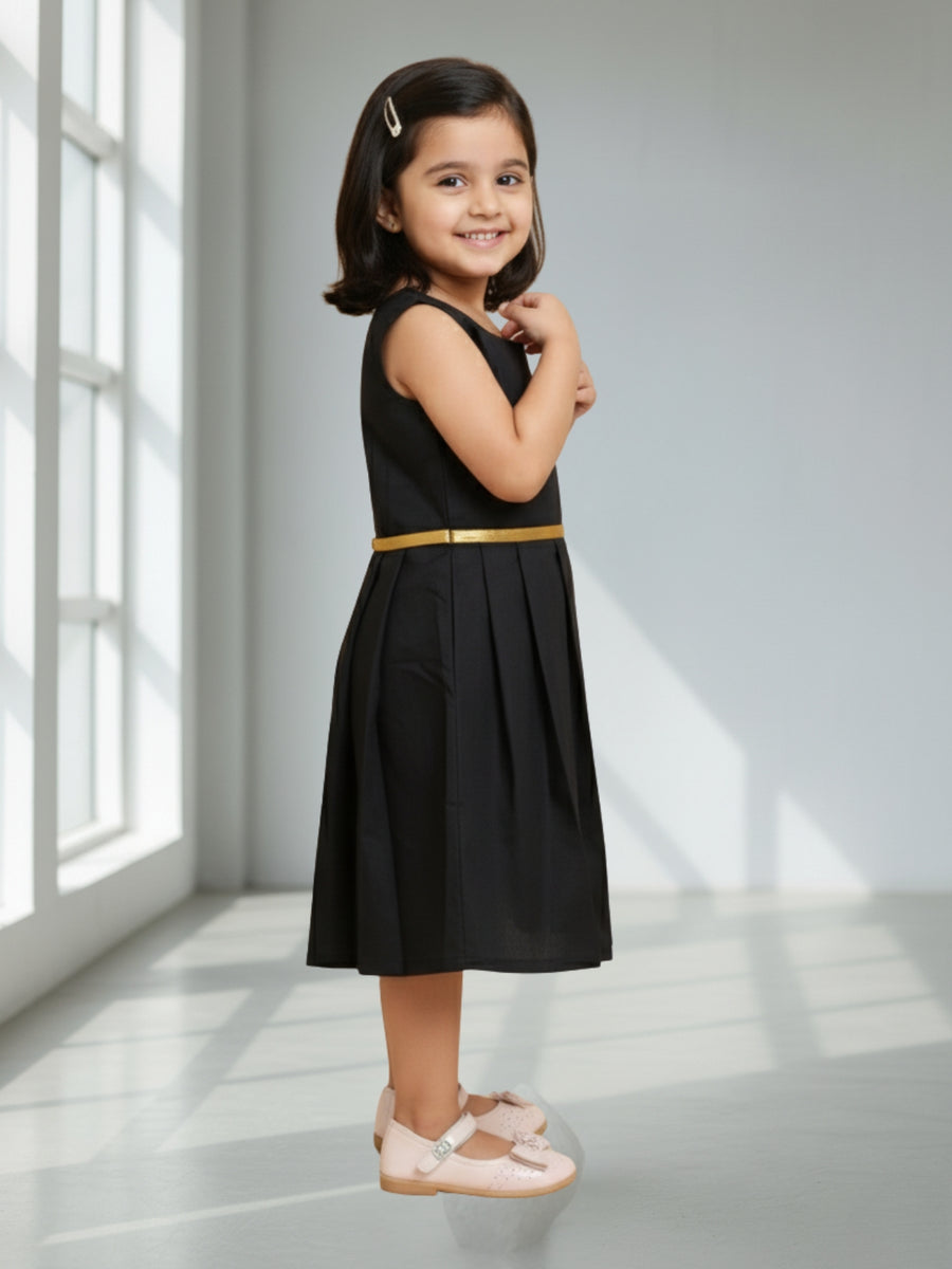 Young girl in a black dress with a gold belt standing in a well-lit room.