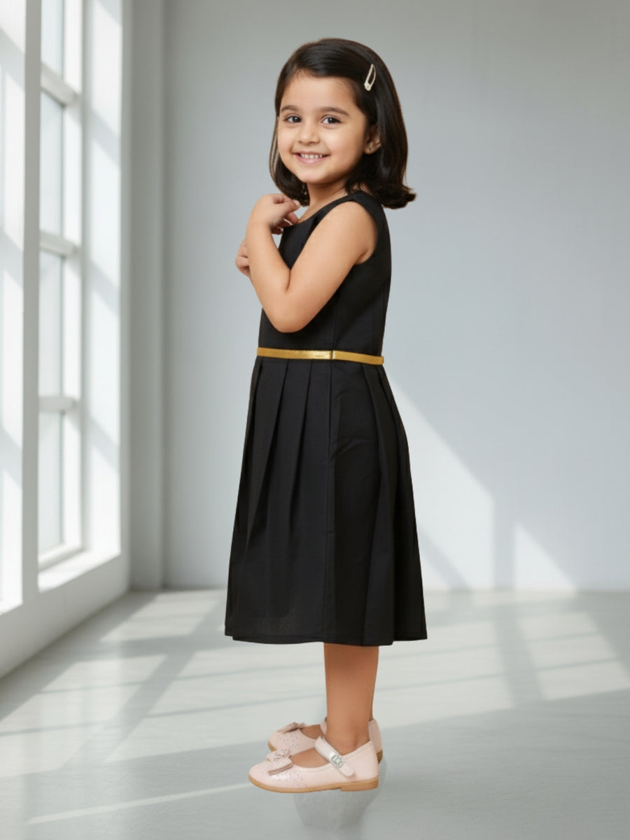 Young girl wearing a black dress with a gold belt in a bright room.