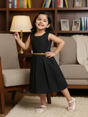 Young girl in a black dress with a gold belt standing in a living room.