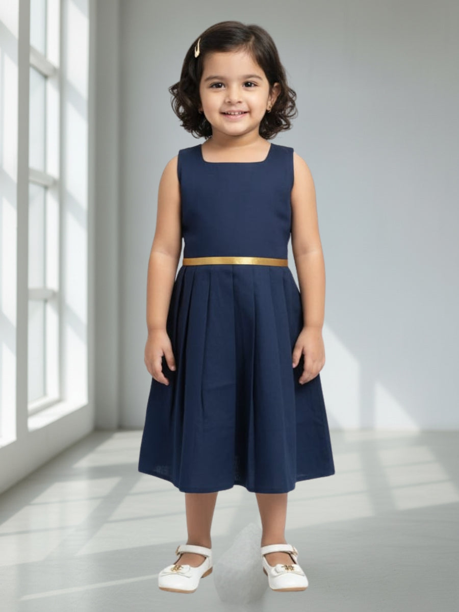 Young girl wearing a navy dress with a gold belt in a bright room.