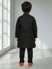 Child wearing a black coat standing in a bright room with sunlight streaming through a window.