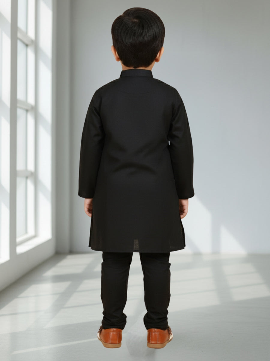 Child wearing a black coat standing in a bright room with sunlight streaming through a window.
