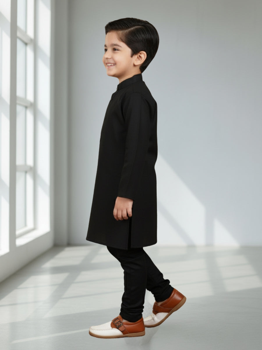 Child wearing a black coat and dark pants standing in a bright room with sunlight streaming in.